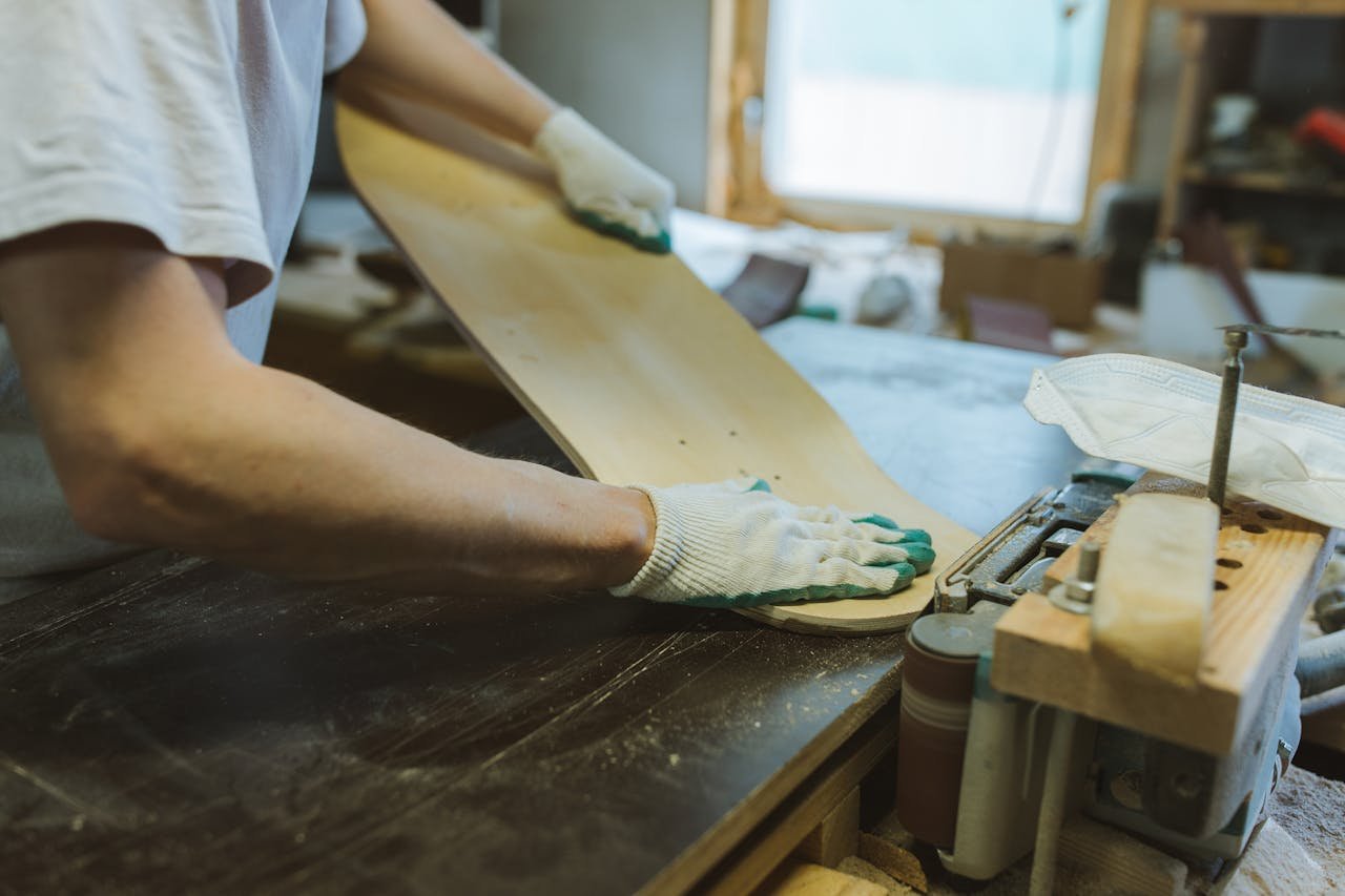 A craftsman meticulously sanding a skateboard deck in an indoor workshop setting.