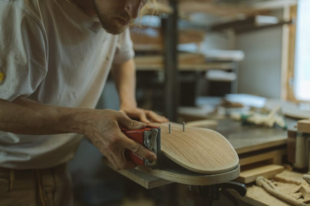 Close-up of a craftsman sanding a skateboard in a home workshop environment.