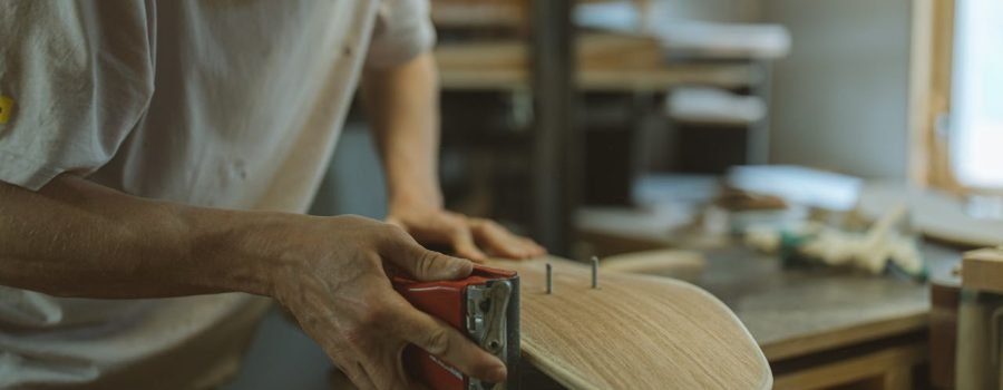 Close-up of a craftsman sanding a skateboard in a home workshop environment.