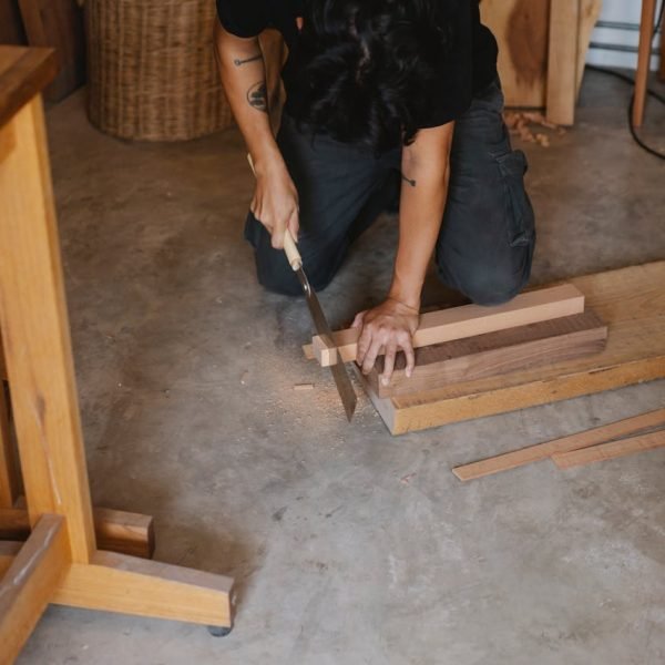 Anonymous joiner working with Japanese saw while cutting edge of timber plank on floor in workshop